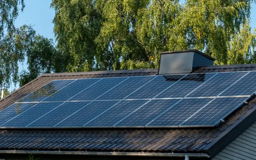 Solar panels on home roof against blue sky and trees
